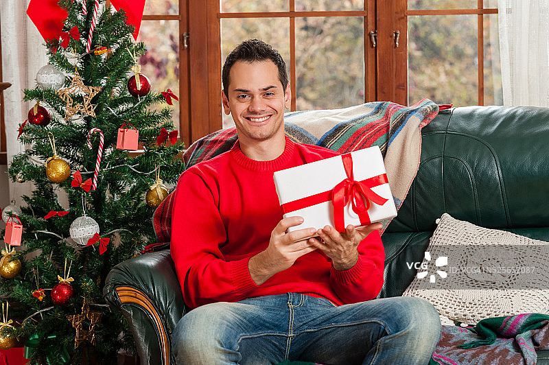 一个年轻人坐在沙发上，在圣诞树前图片素材
