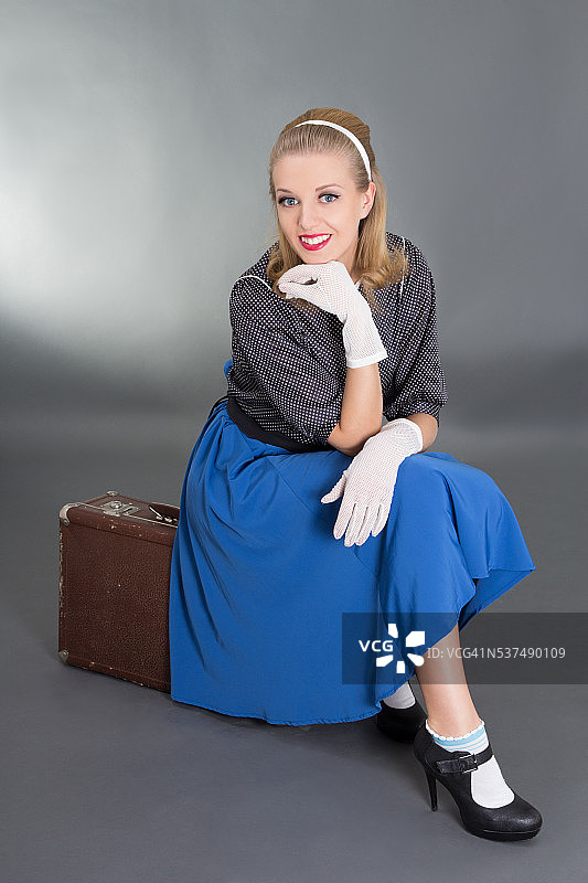 年轻漂亮的海报女郎坐在复古行李箱上图片素材