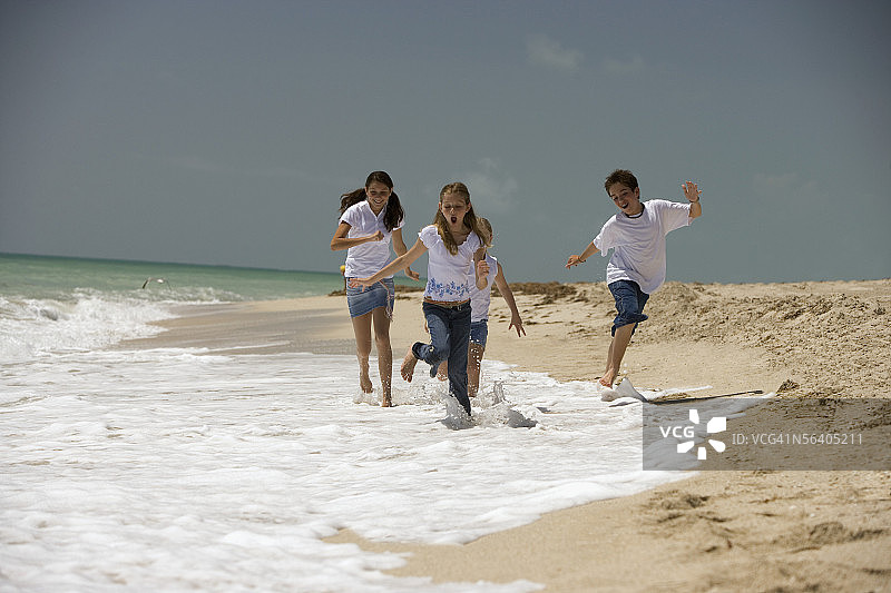 男孩和三个女孩在沙滩上跑步图片素材