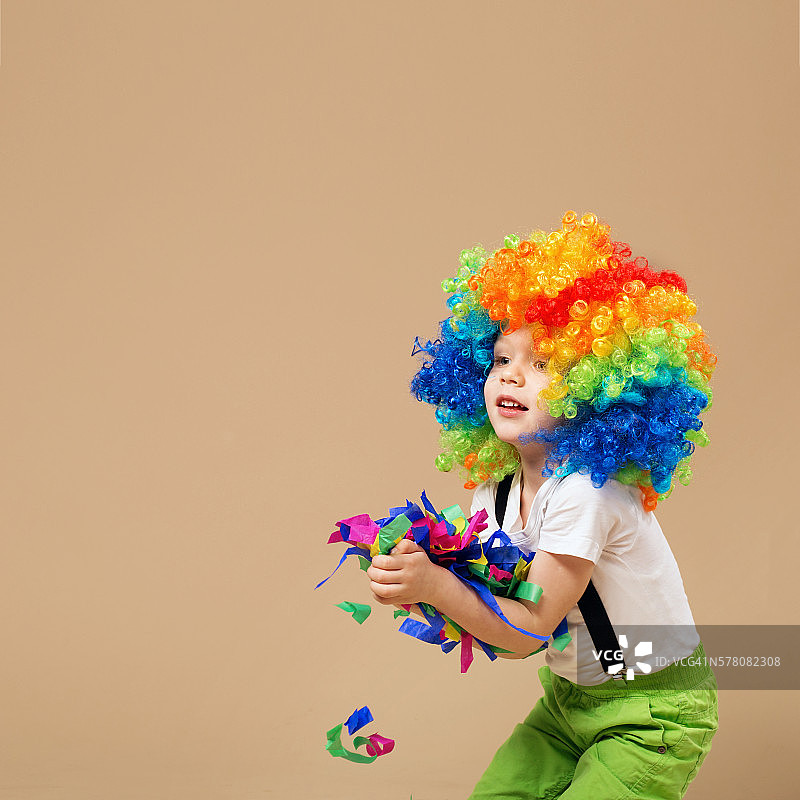 快乐的小丑男孩戴着五颜六色的大假发。图片素材