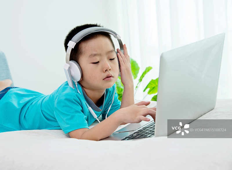 小男孩戴着耳机在沙发上使用笔记本电脑图片素材