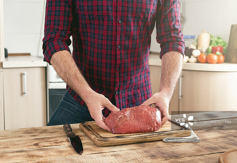 一个男人拿着一块新鲜的牛肉放在木桌上图片素材