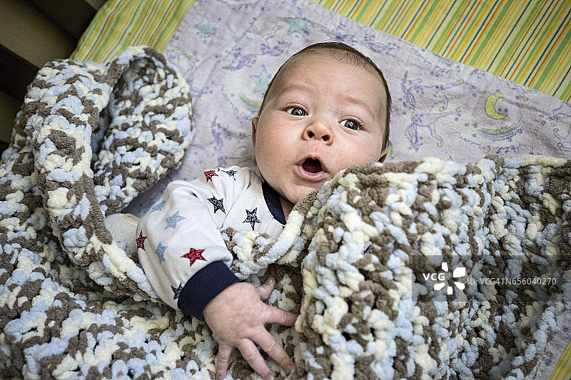 婴儿在婴儿床上移动的毯子有有趣的表情。图片素材