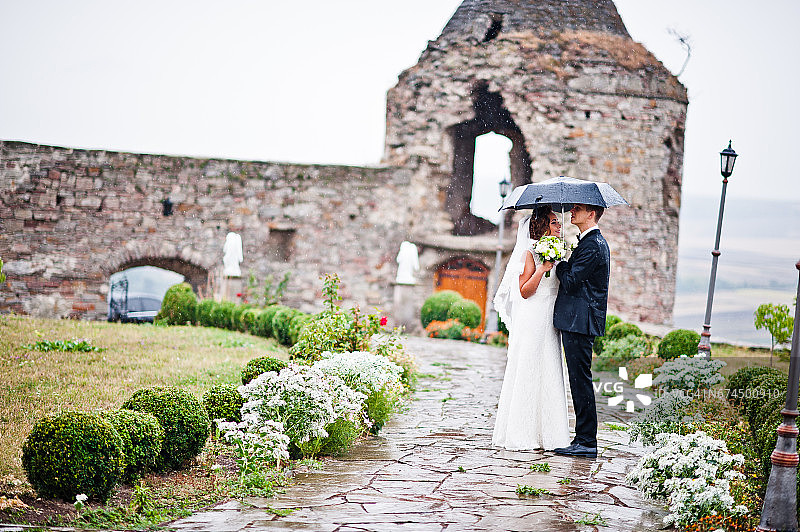 新婚夫妇在雨中带着伞漫步古塔的背景城堡图片素材