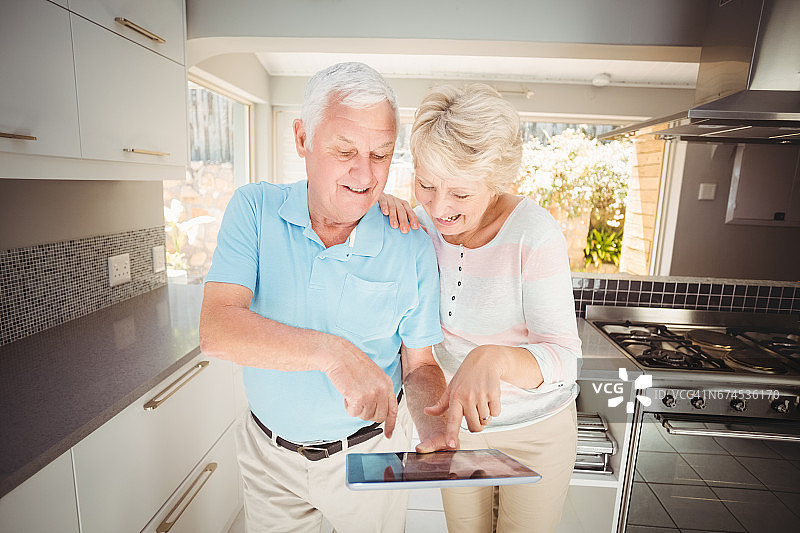 快乐的老年夫妇在厨房里拿着平板电脑图片素材