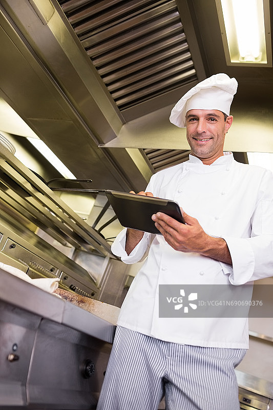 微笑的男性厨师在厨房使用数码平板电脑图片素材