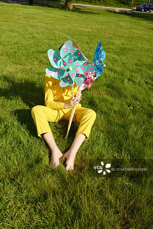 年轻的女孩在草地上玩黄色的连身衣和风车图片素材