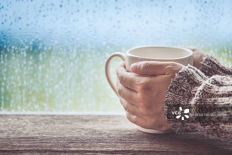 女人手拿着一杯咖啡或茶在雨天的窗户背景图片素材