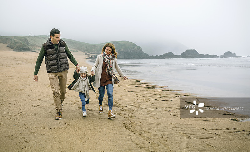 一个幸福的家庭和女儿在冬天的海滩上散步图片素材