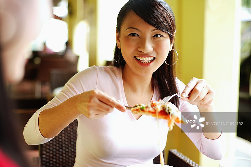 一名年轻女子用刀叉拿起一片披萨，对着面前的另一个人微笑图片素材