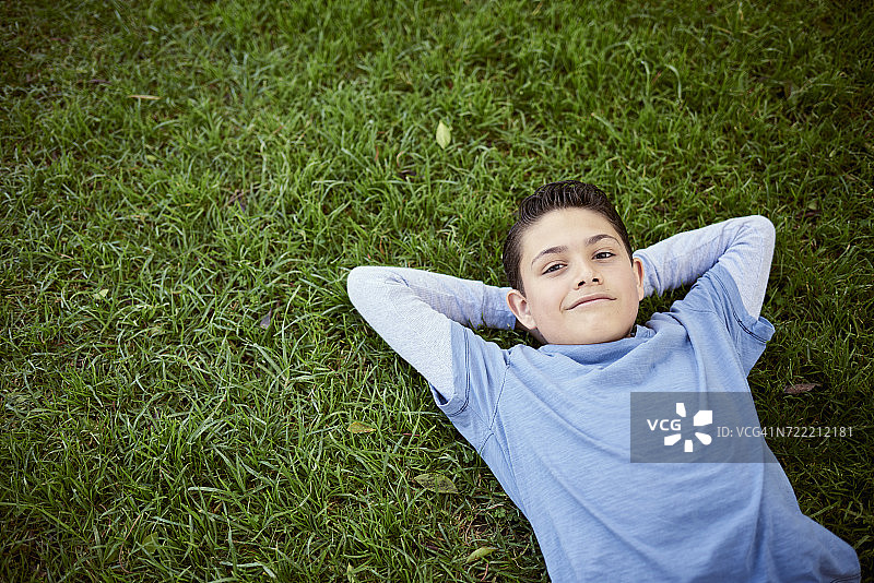 微笑的西班牙男孩躺在草地上图片素材