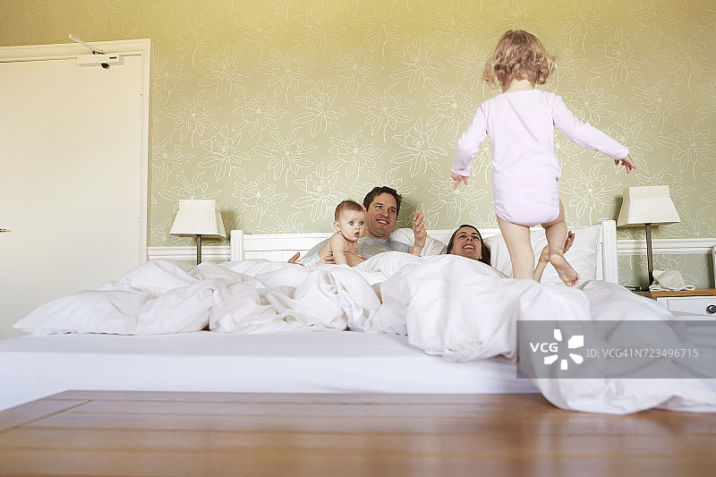 女婴与父母和小妹妹一起踩在床上图片素材