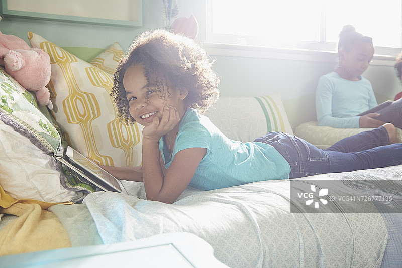 微笑的黑人女孩的肖像躺在床上使用数字平板电脑图片素材