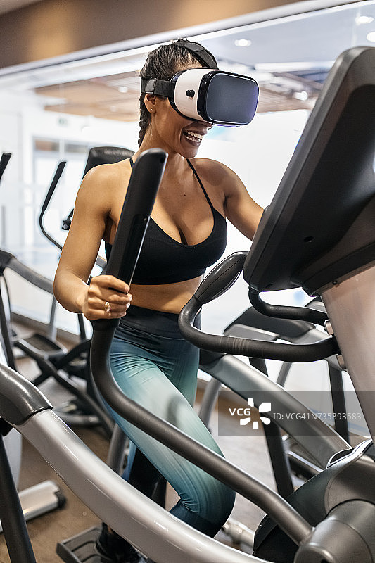 戴着虚拟现实眼镜在健身房椭圆训练的女人图片素材