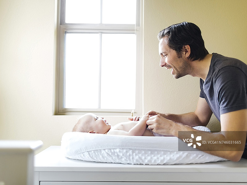 父亲和男婴(12-17个月)在换垫子上玩耍图片素材