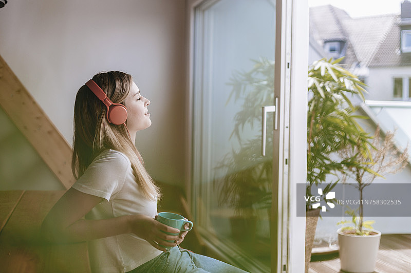 年轻女子在家里悠闲地喝着茶，听着音乐图片素材