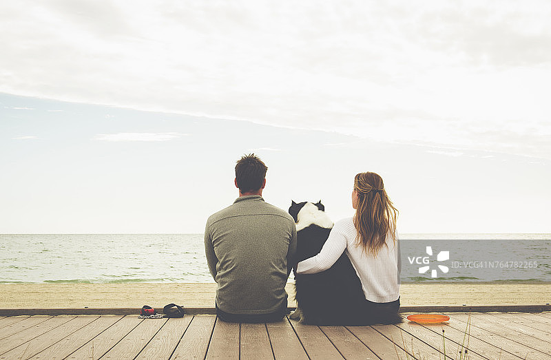 一对白种人夫妇和一只狗坐在海边的木板路上图片素材