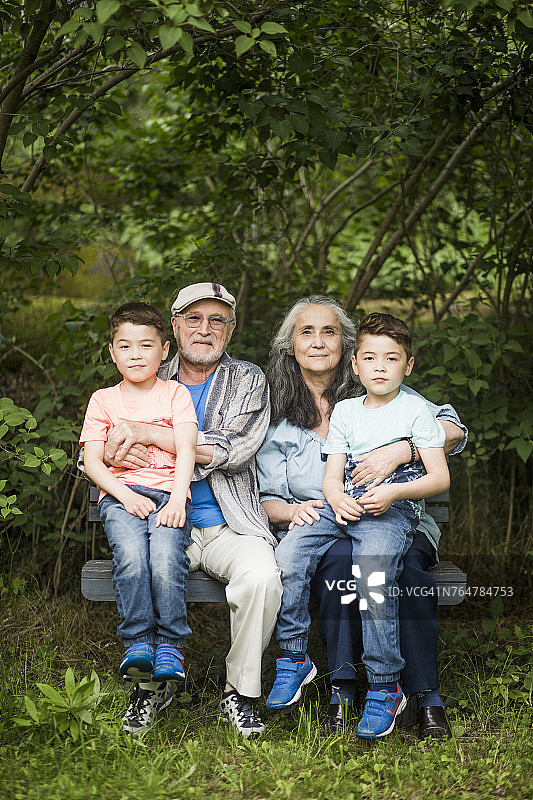 祖父母和双胞胎孙子坐在后院靠植物的长凳上的肖像图片素材