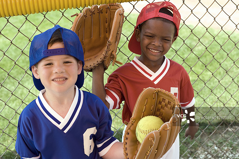 穿着棒球服的男孩戴着手套站在篱笆旁图片素材
