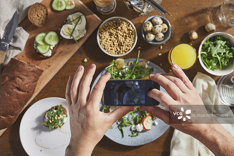 用手机拍摄餐桌上食物的人的裁剪图像图片素材