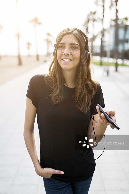 微笑的年轻女子在木板路听音乐图片素材