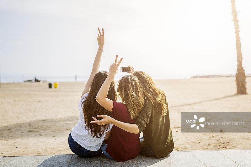 三个女性朋友坐在海滩自拍的后视图图片素材