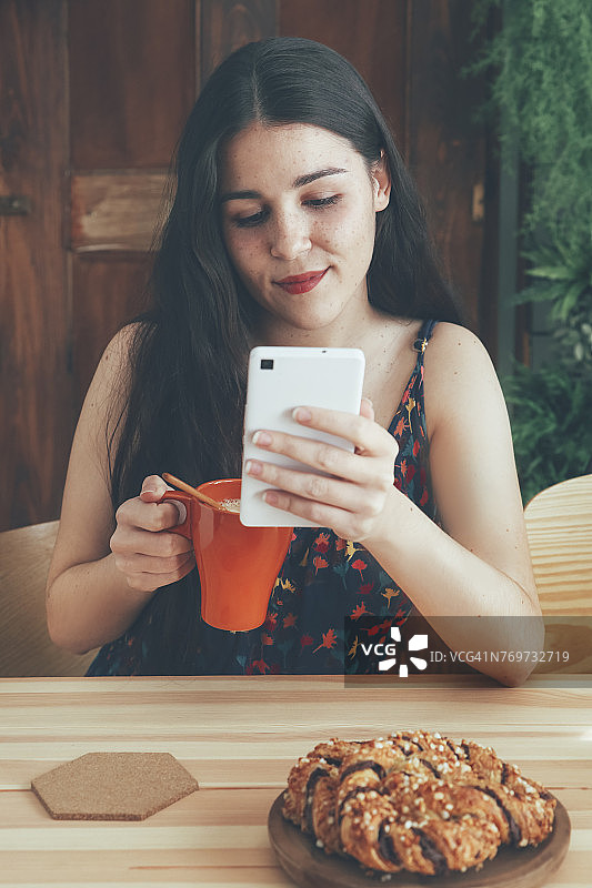 满脸雀斑的年轻女子，拿着咖啡杯用智能手机图片素材