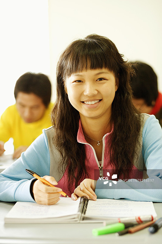 一名年轻女子的肖像坐在教室的一张桌子前，微笑着图片素材