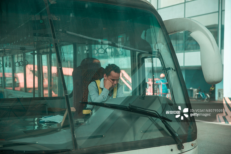 越南河内，一名机场巴士司机在上班时间边开车边打盹。图片素材