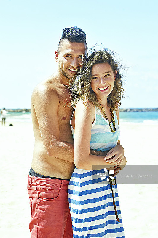迷人的年轻夫妇微笑着站在阳光下的海滩在一个夏天的一天图片素材