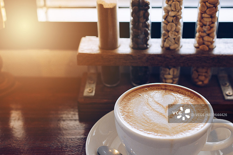 近距离的一杯热拿铁咖啡在木桌上与一个咖啡豆在玻璃管在背景。图片素材