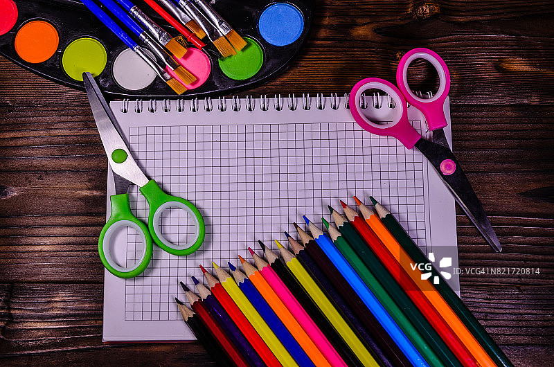 一套不同的文具。笔记本，剪刀，铅笔，颜料，画笔放在木桌上。回到学校。俯视图图片素材