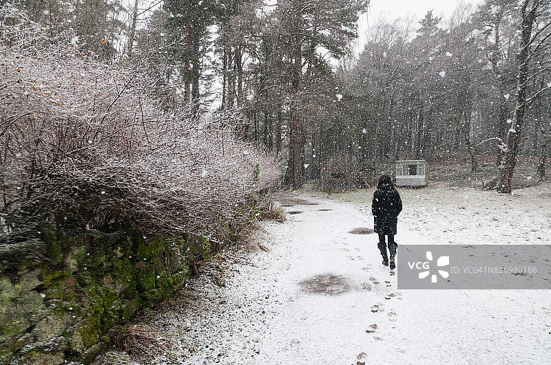 女孩穿着黑衣走在铺满雪的小路上图片素材