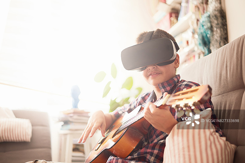 一个小男孩一边弹吉他一边看虚拟现实图片素材