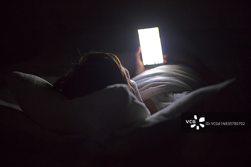 深夜躺在床上用智能手机搜索社交媒体的女人，上网成瘾。图片素材
