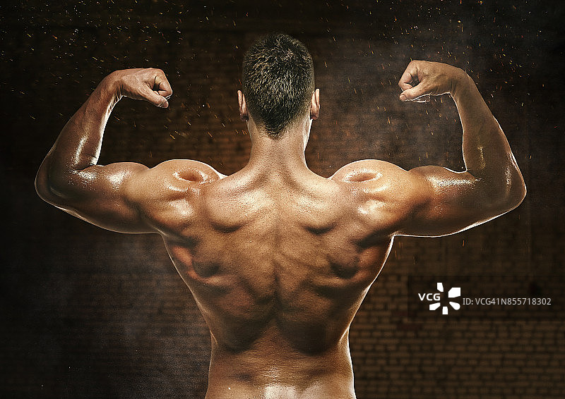 一个肌肉发达的健身者的背部弯曲的照片，拍摄的背景是黑色的砖图片素材