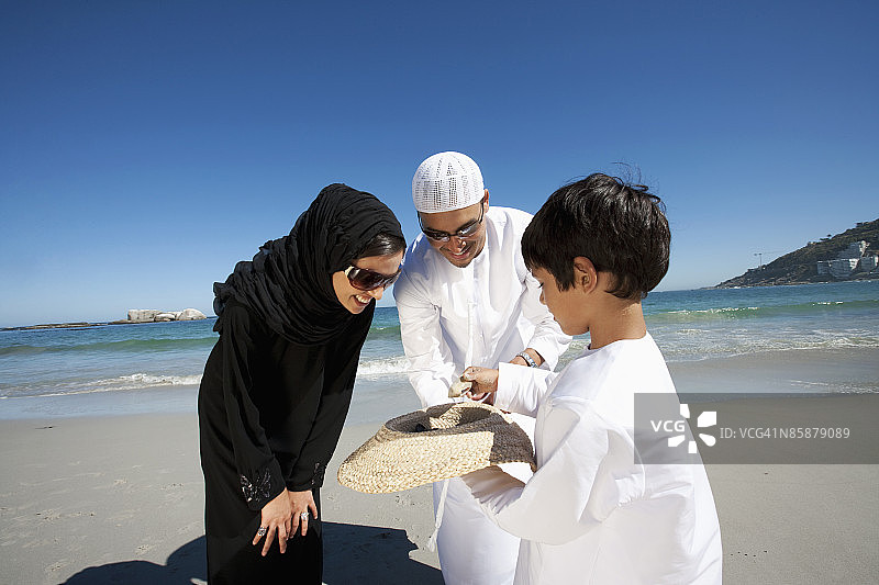 阿拉伯父母带着儿子看着帽子里的贝壳。图片素材