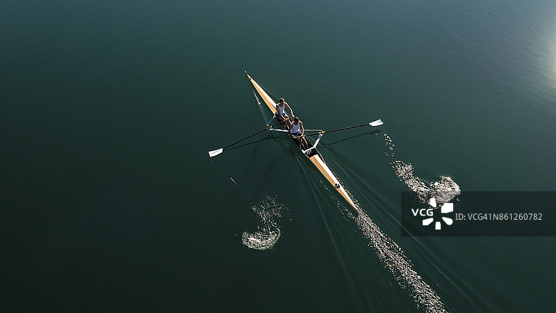 两名男运动员在阳光下在湖上划桨图片素材