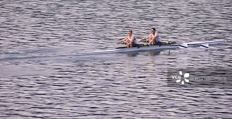 下午晚些时候，两名男运动员划船穿过湖面图片素材