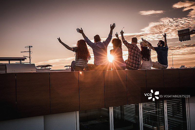 一群朋友在屋顶上玩在日落的后视图。图片素材
