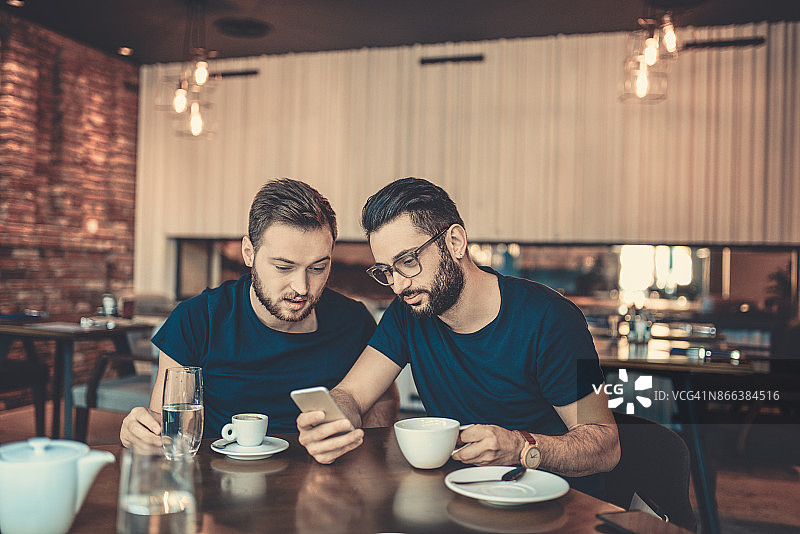 两个笑着看智能手机的朋友在咖啡馆餐厅图片素材