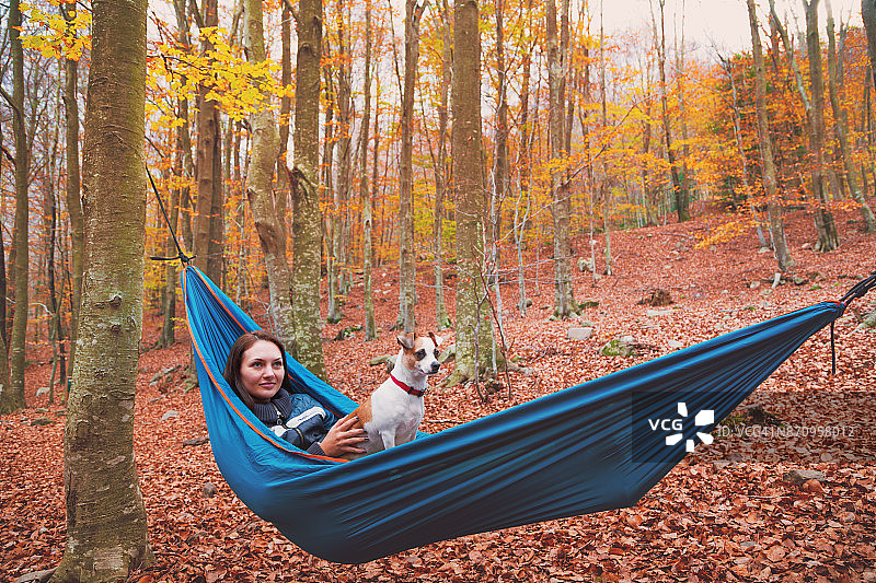 快乐的女人在美丽的森林里享受秋天的季节在Montseny山旅行期间，与狗，在一个独特的地方，在一个自然之间摇摆的吊床上休息，凝视美丽的树木。图片素材