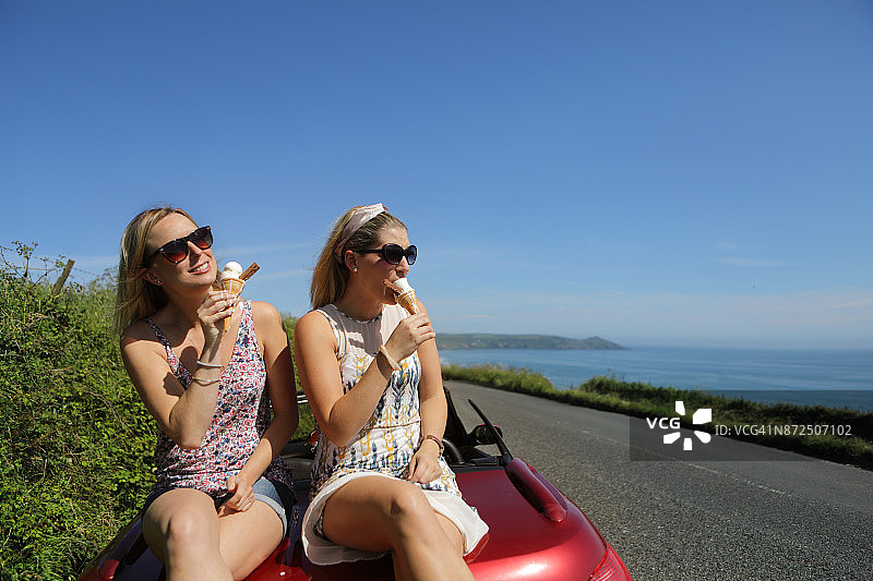 两个女人坐在海边的汽车上吃冰淇淋图片素材