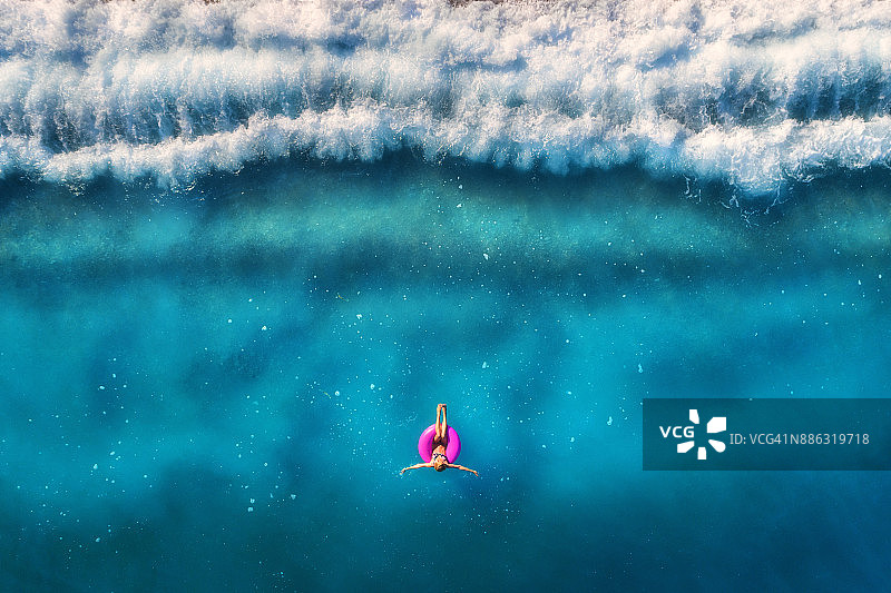 鸟瞰图上的年轻女子游泳在粉红色的游泳圈在透明的绿松石海Oludeniz，土耳其。夏日的海景与少女，美丽的海浪，蔚蓝的海水在日出。无人机俯视图图片素材