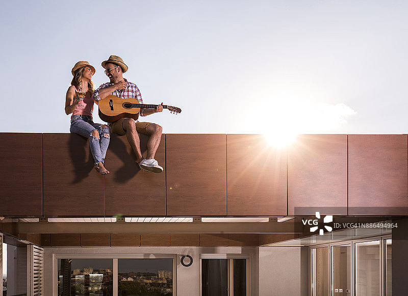 相爱的年轻夫妇享受在一个屋顶上的原声吉他。图片素材