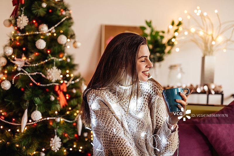 一个女人在圣诞节期间喝着咖啡，背景是她的圣诞树图片素材
