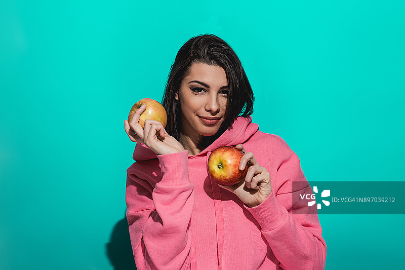 一个年轻女子拿着一个苹果，站在一个蓝色的背景图片素材