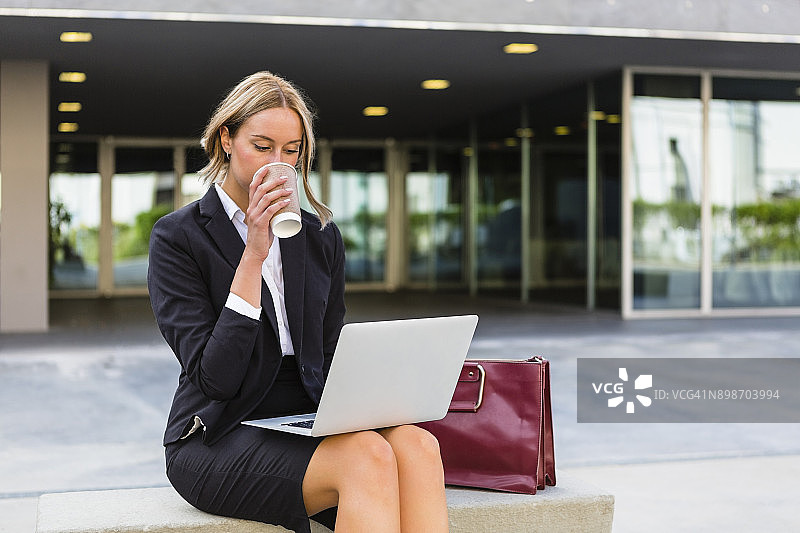 女商人带着时尚的皮包和咖啡坐在长椅上看笔记本电脑图片素材