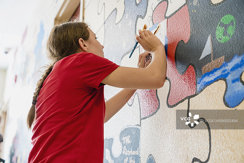 一个白人女孩在学校墙上画壁画图片素材