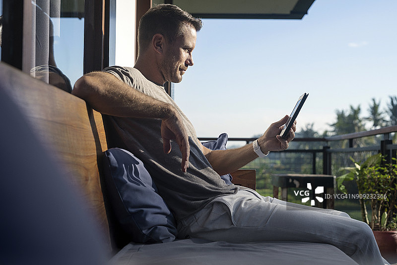 男人坐在现代房子的阳台上，看着智能手机图片素材